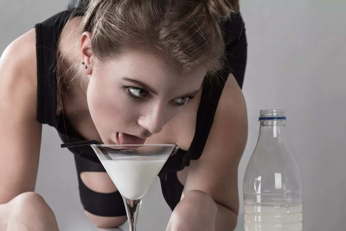 A woman lying on her back drinking a glass of milk like a cat